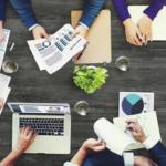 4 Benefits of Web Accessibility business marketing meeting - people sitting around a table covered in charts, papers, and laptops