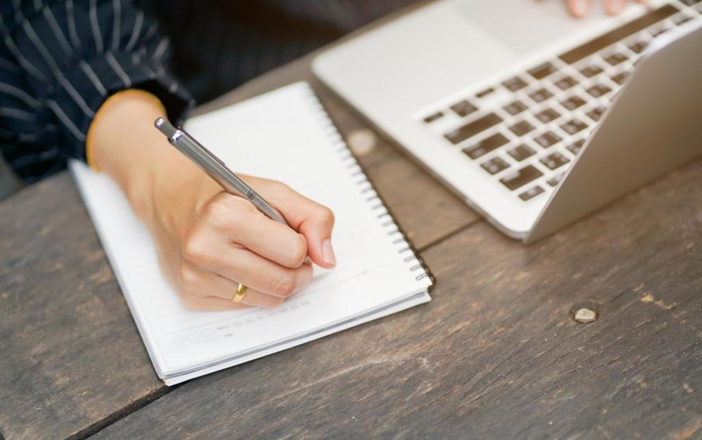 person writing on notebook next to a laptop