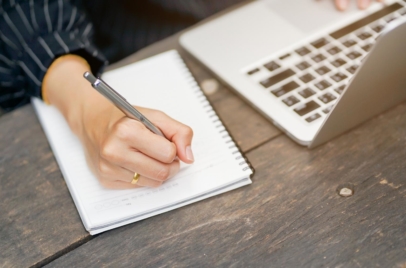 person writing on notebook next to a laptop