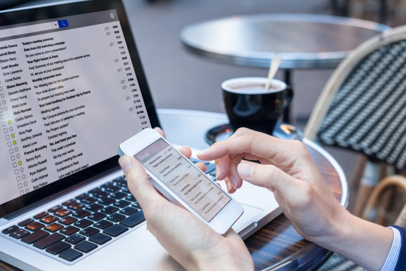 businessperson checking email on phone and laptop