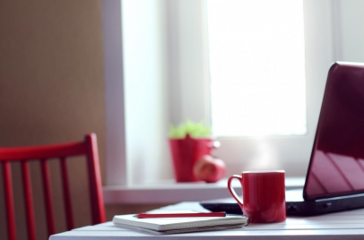 laptop, notebook, and coffee mug on a table with red chair - work from home concept