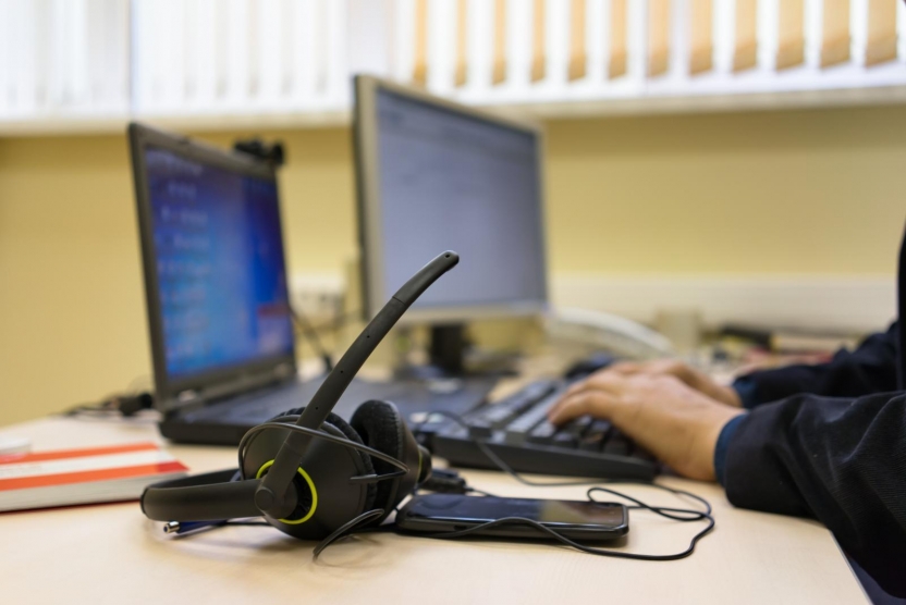 headset on a desk with a person typing on a laptop