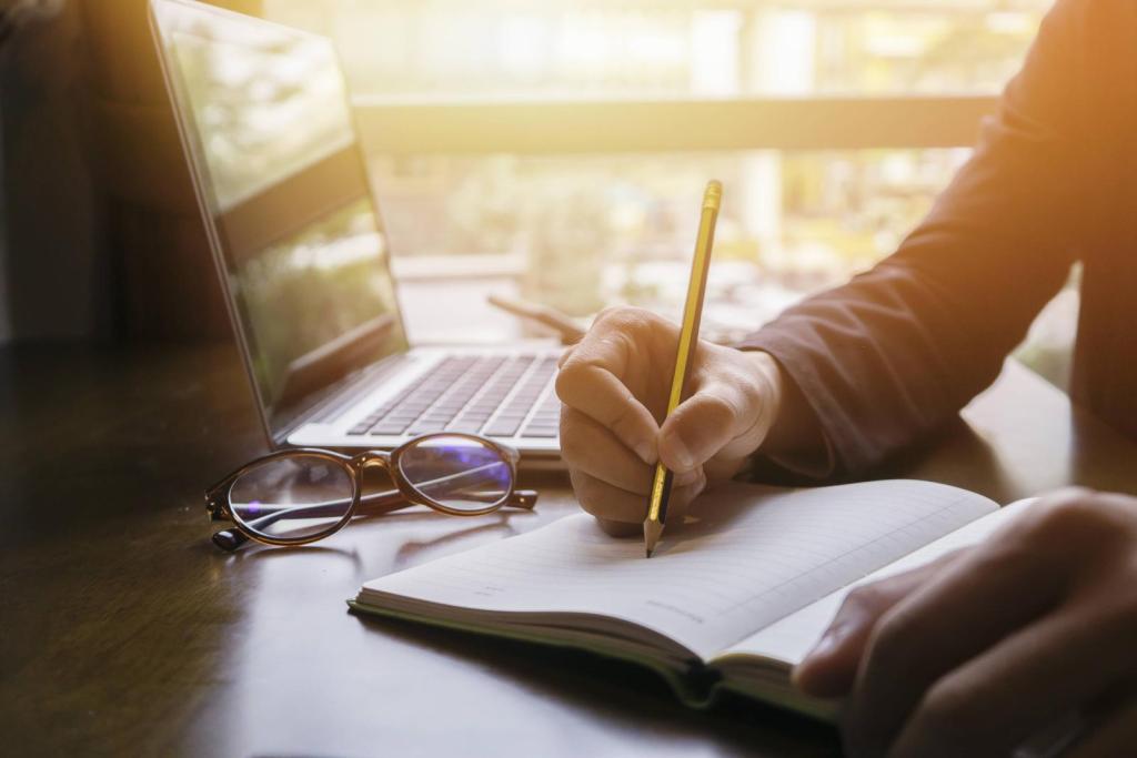 person writing in a notebook next to a laptop