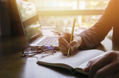 person writing in a notebook next to a laptop