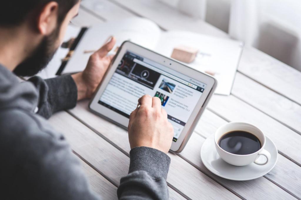 man navigating a website on a tablet next to an open notebook and a cup of coffee