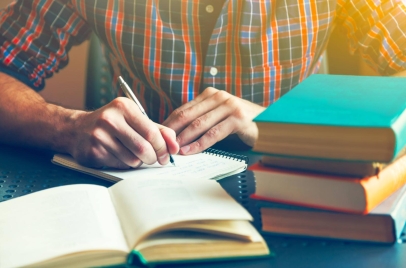 man writing in notebook with a stack of books