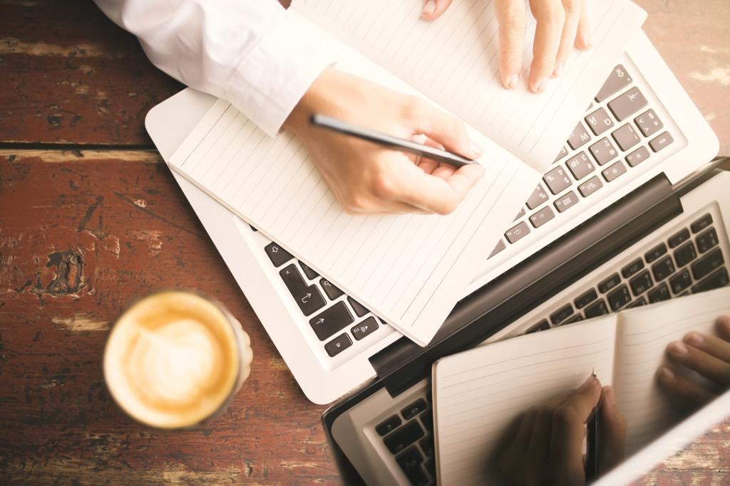 a person writing on paper and laptop computer