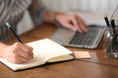 person writing on laptop and pad of paper