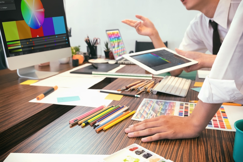 web design vs print design concept - artists brainstorming colors with screens and papers