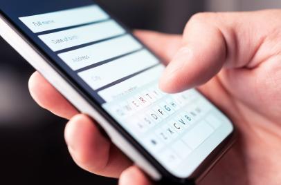 hand holding a cell phone and using it to fill out a website form