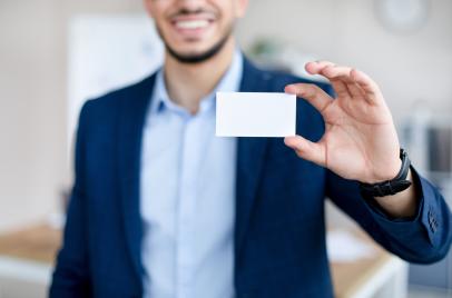 Cropped view of young Arab man showing empty business card with mockup for design at modern office.