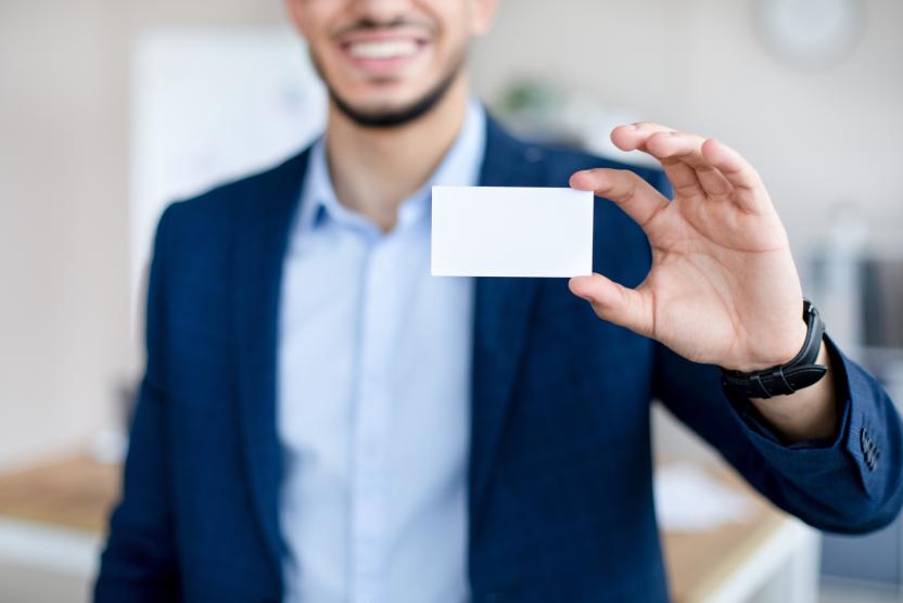 Cropped view of young Arab man showing empty business card with mockup for design at modern office.