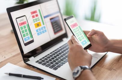 man holding phone and looking at website on phone and laptop
